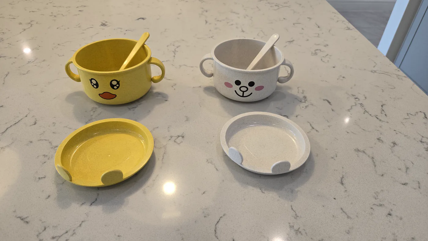 Yellow duck and oat bear bowls with two matching spoons and two lids laid out as plates